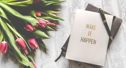 Photo of a journal that says make it happen, a pen, and some red tulips
